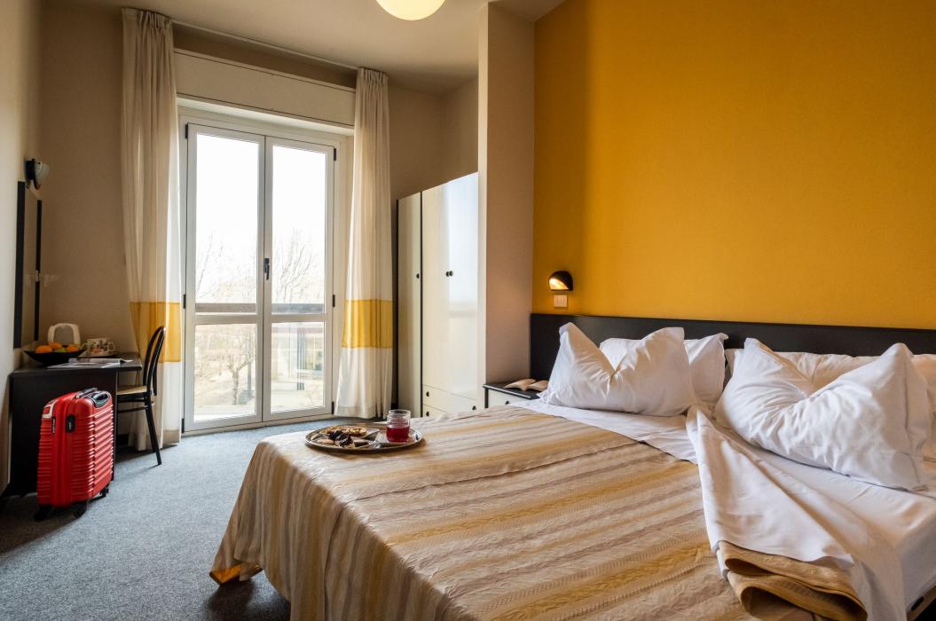 Camera accogliente con pareti gialle, letto comodo e luce naturale da ampie finestre.