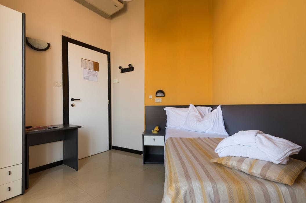 Camera d'albergo accogliente e luminosa, con letto ordinato e pareti colorate.