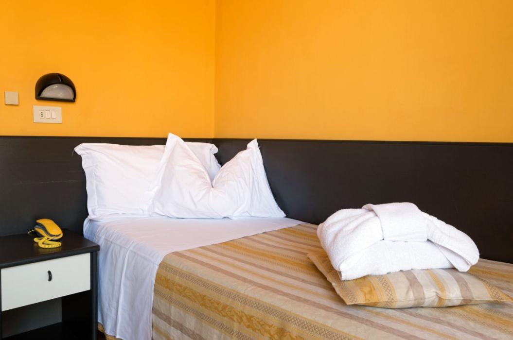 Camera accogliente con letto singolo, pareti gialle, telefono vintage e accappatoio piegato.
