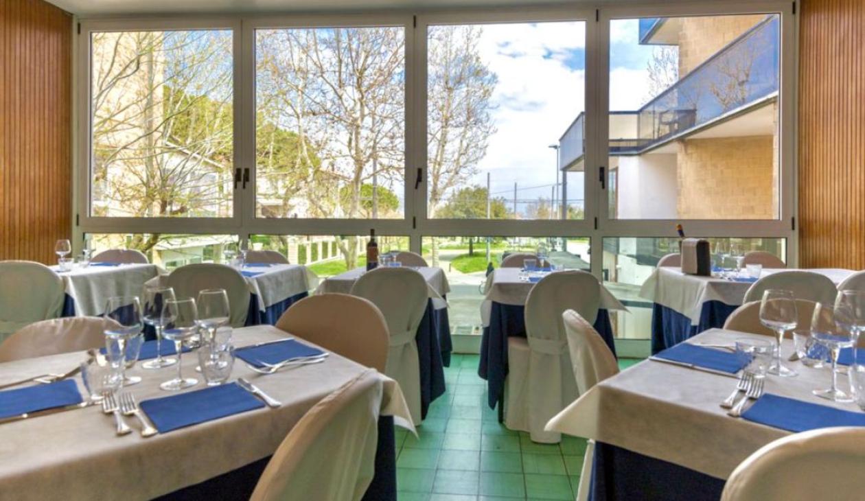Ristorante luminoso, tavoli eleganti, vista su giardino verde e cielo azzurro.