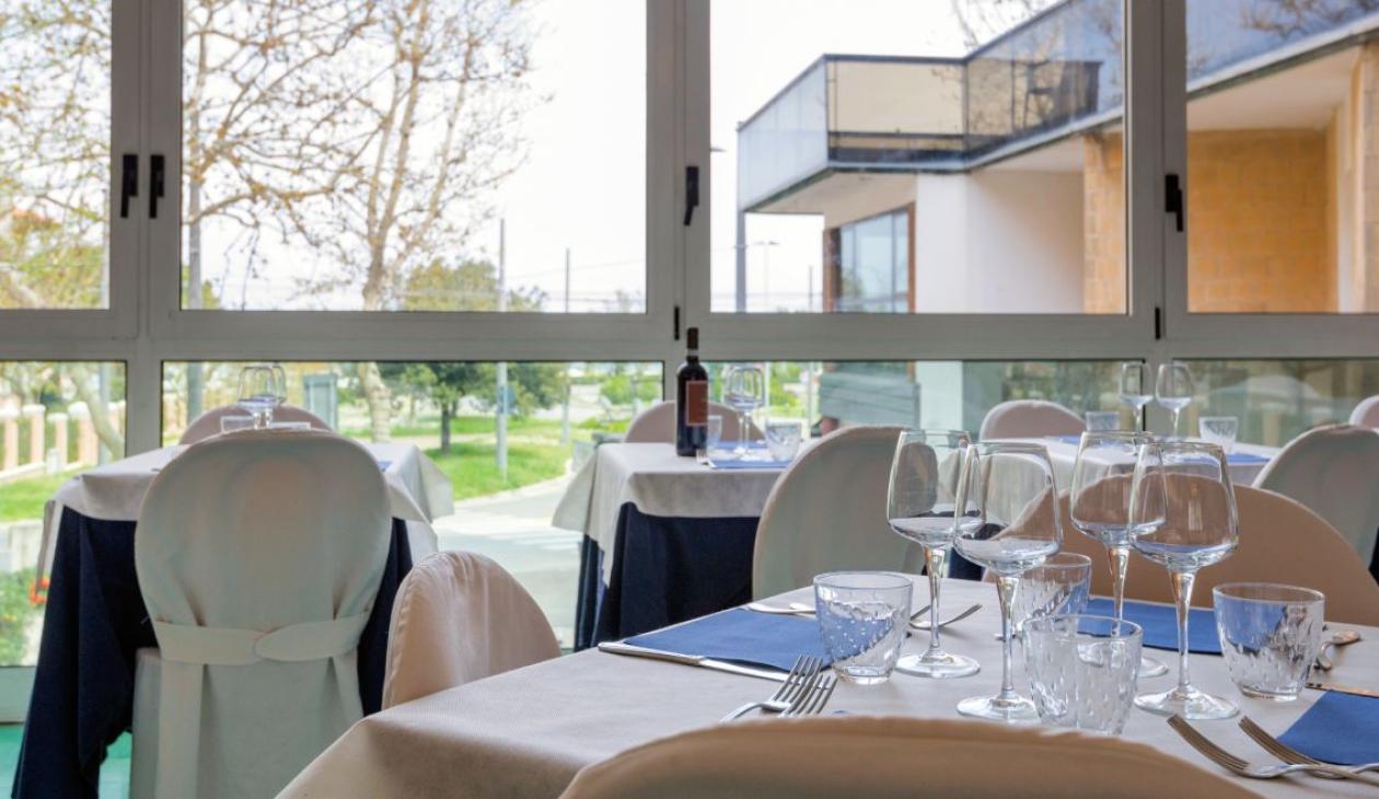 Ristorante elegante, tavoli apparecchiati con cura, ampie finestre, vista su giardino verde e moderno.