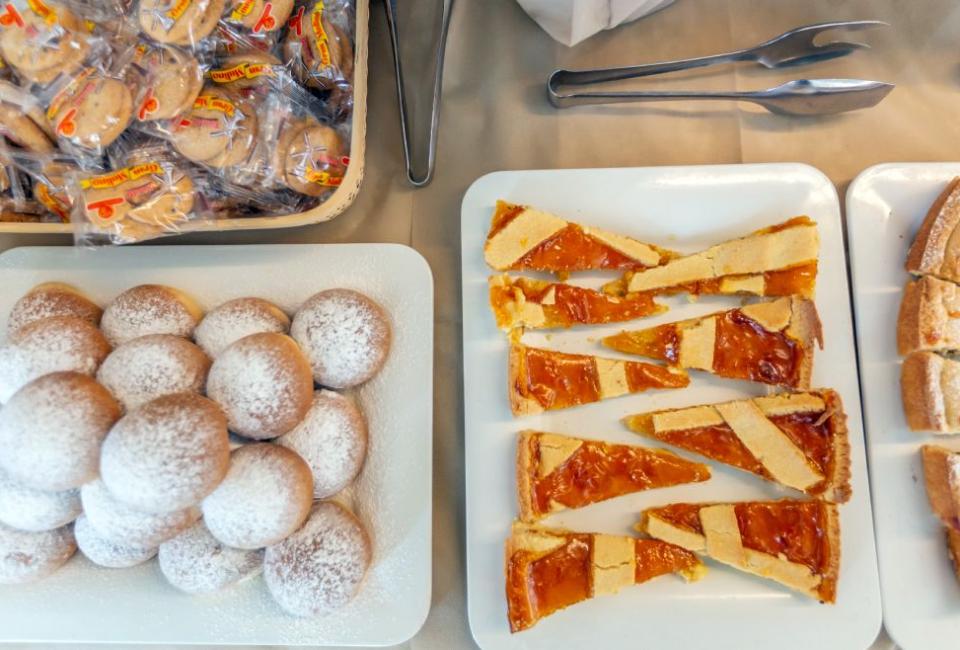 Dolci invitanti su piatti: crostate, biscotti confezionati e soffici bomboloni con zucchero a velo.